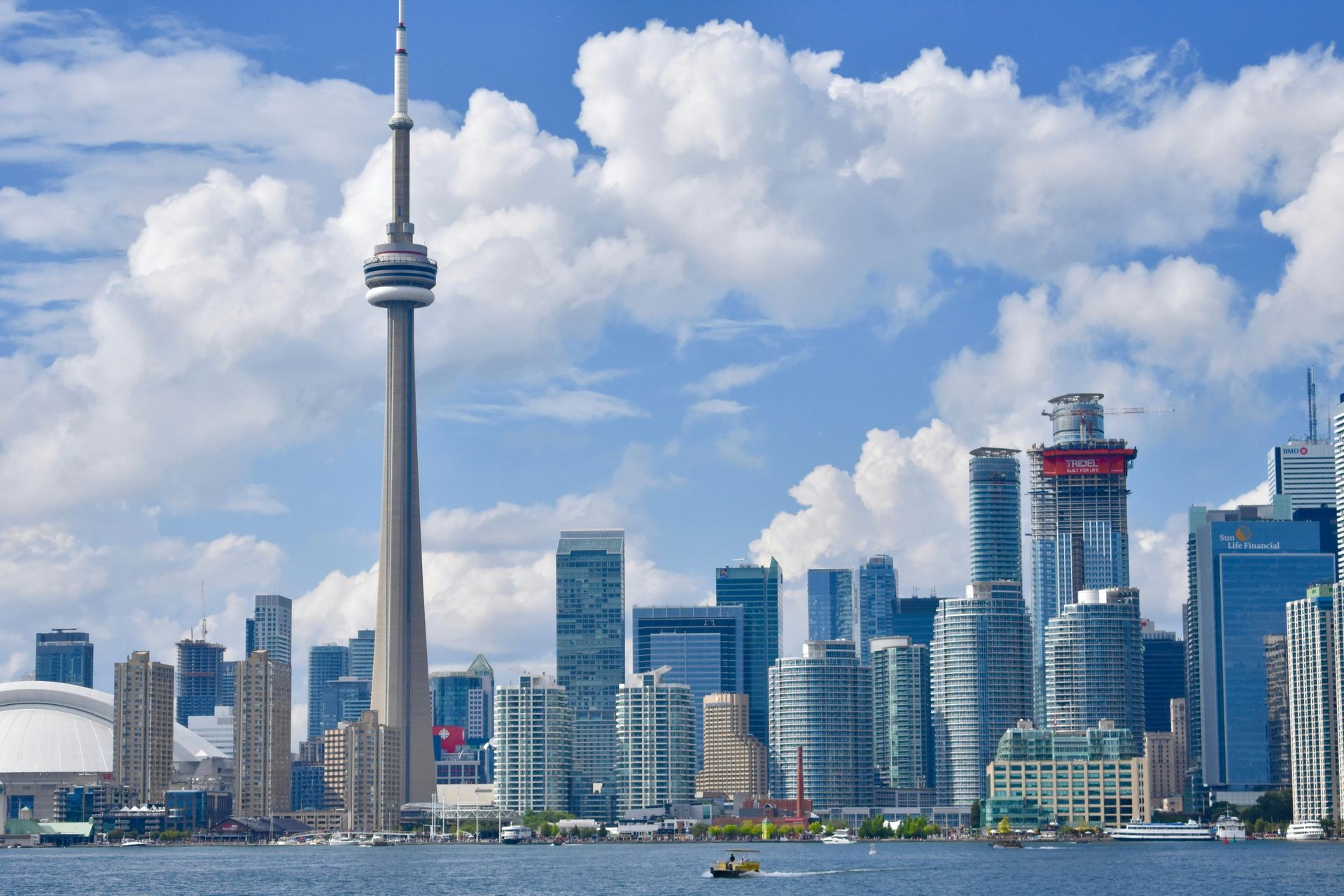 Toronto skyline featuring the CN Tower and modern buildings under a bright sky with scattered clouds.