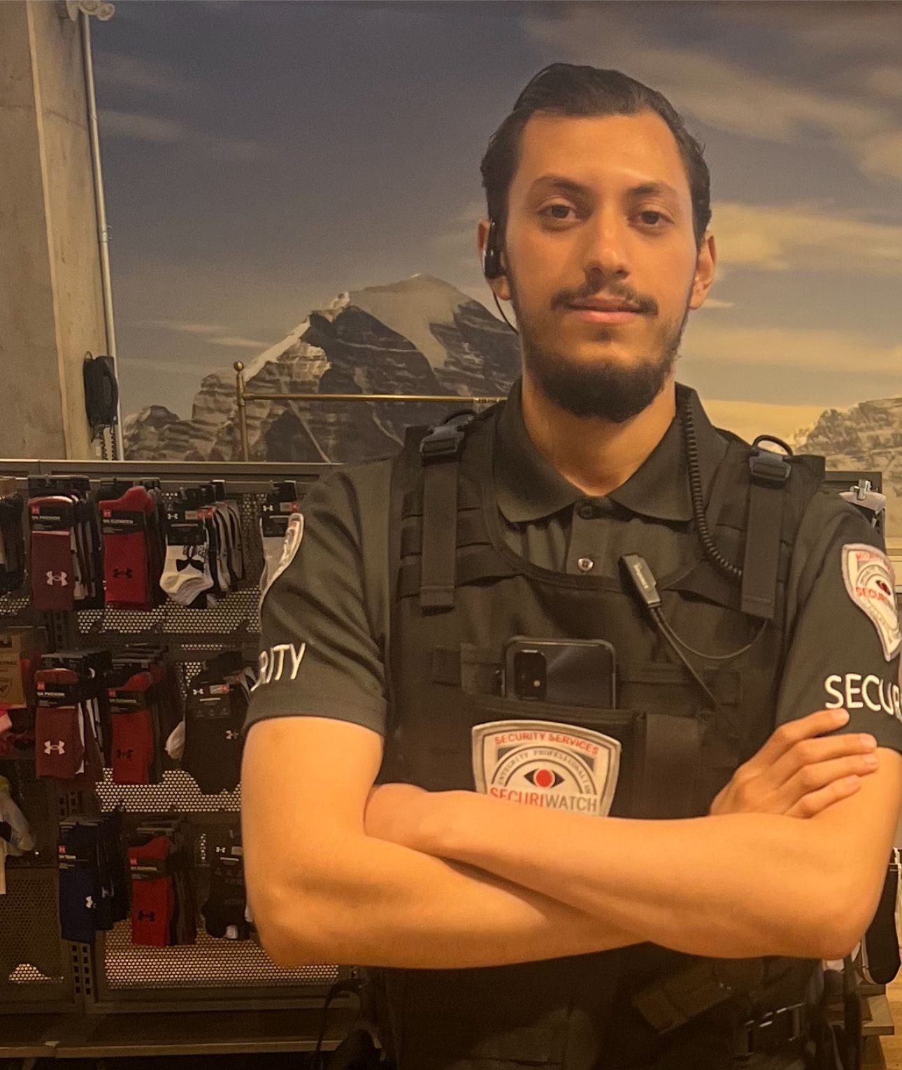 Security guard in uniform standing with arms crossed in front of a display wall filled with athletic socks.