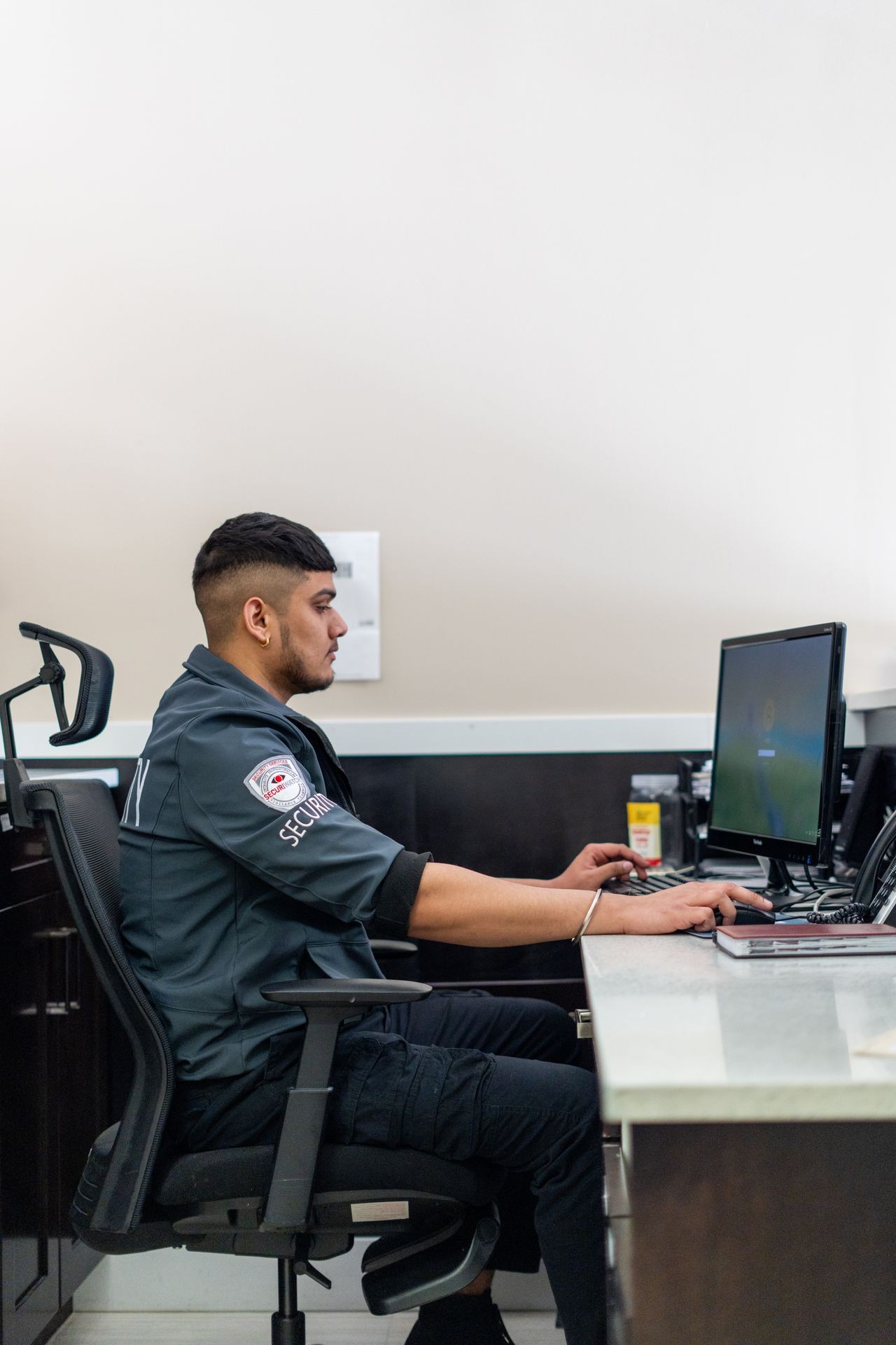 Security guard sitting in a chair at a desk, working on a computer in an office environment.