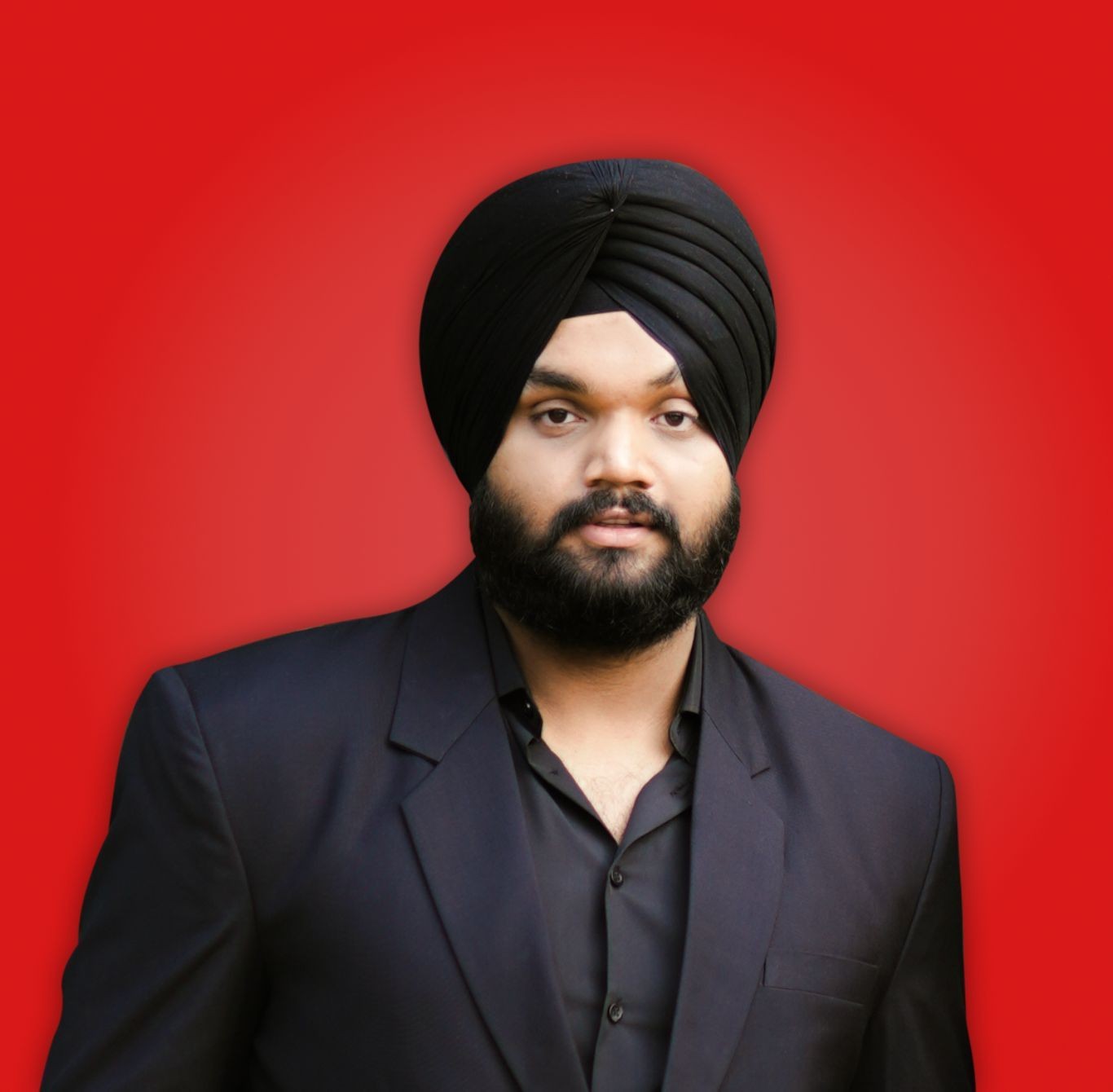 Man wearing a black turban and suit, posing against a vibrant red background.