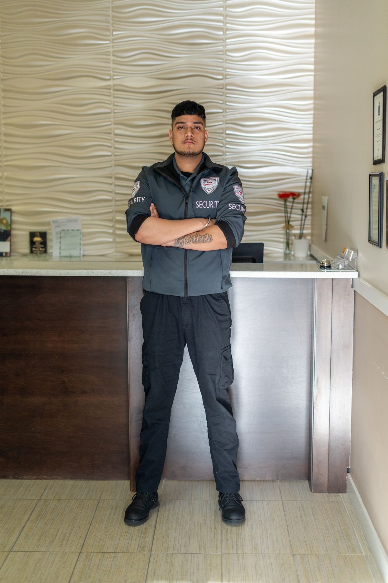 Security guard standing with crossed arms in front of a reception desk with wavy wall design.