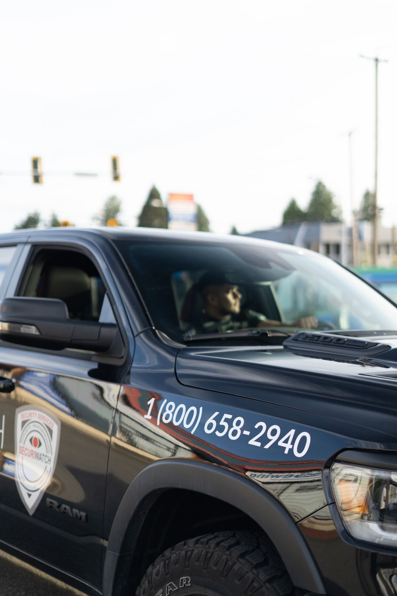 Security vehicle with company logo and phone number parked on the street with a security guard visible inside.