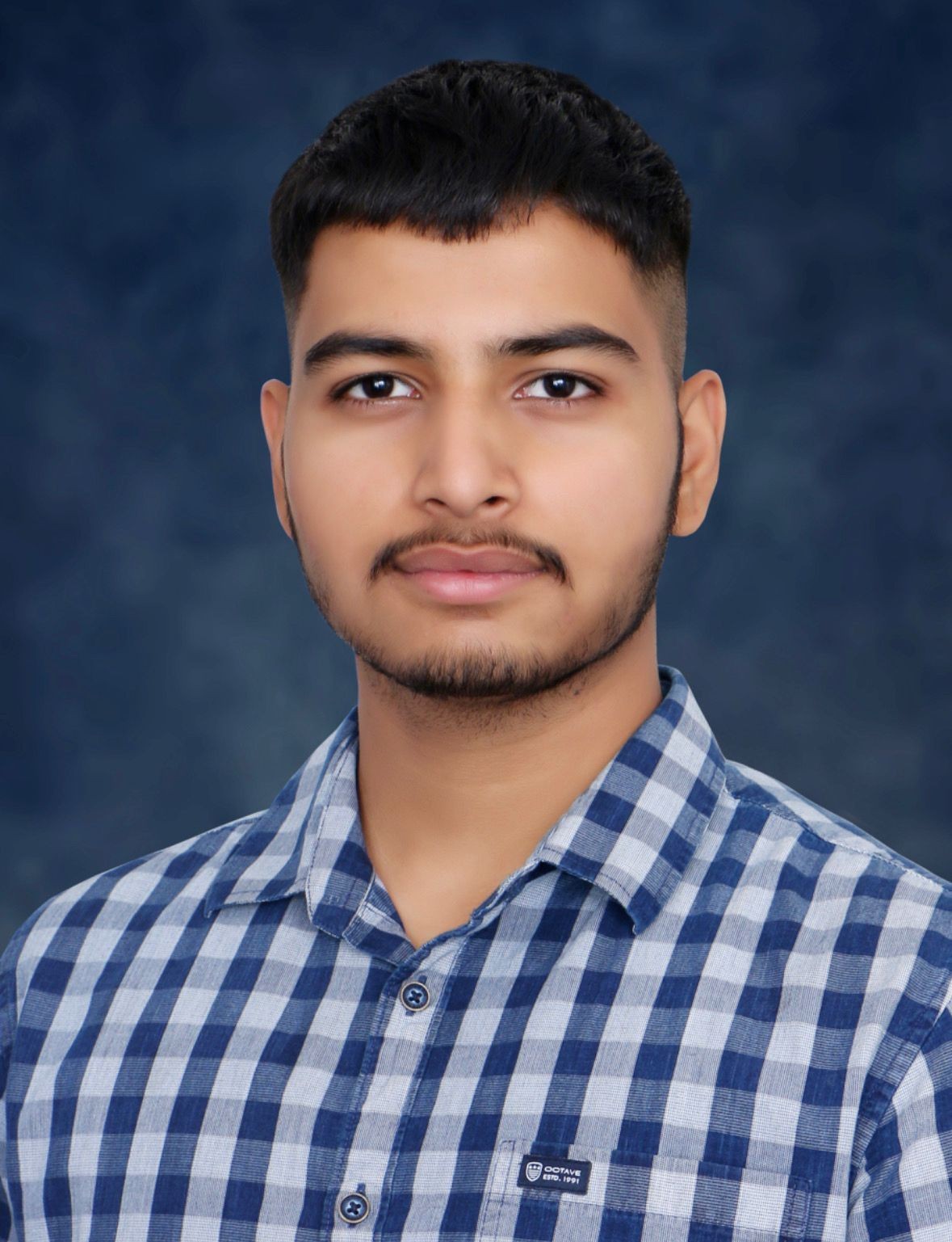 Person wearing a blue and white checkered shirt, standing against a blue textured background.