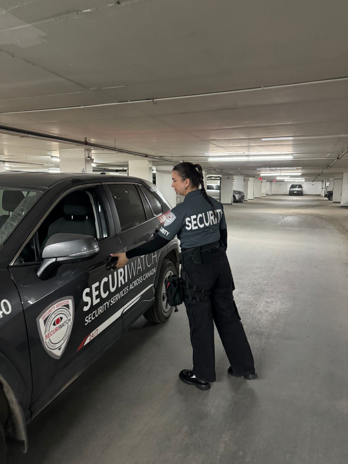 Security personnel standing next to a SecuriWatch vehicle in an underground parking garage.