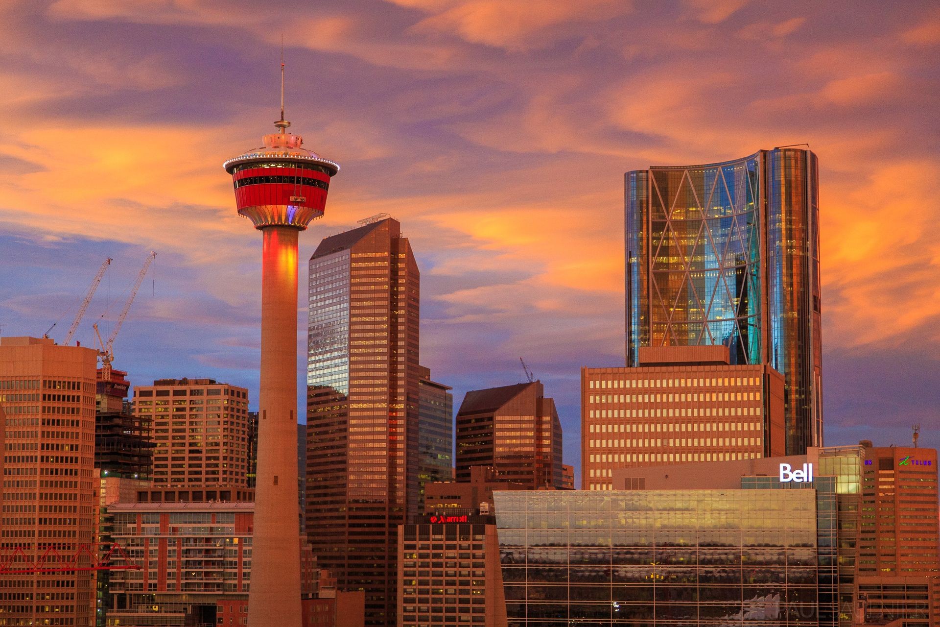 Calgary city skyline at sunset featuring the Calgary Tower and modern skyscrapers against a colorful sky.